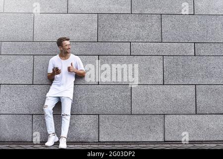 Portrait of a handsome young man in casual clothes enjoying music on your mobile phone, against a brick wall Stock Photo