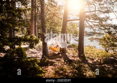 Mature man relaxing in hammock at lakeshore during sunny day Stock Photo