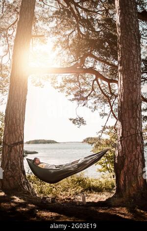 Man sleeping in hammock at lakeshore Stock Photo