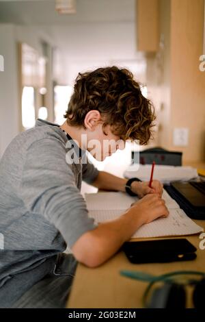 Boy writing in book while doing homework sitting at table Stock Photo