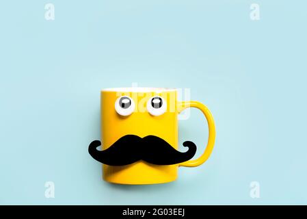 Happy Father's Day.Yellow mug with mustache and funny eyes looking up and copy space on a blue background Stock Photo