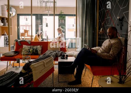Mature man using digital tablet with woman and daughter in background Stock Photo