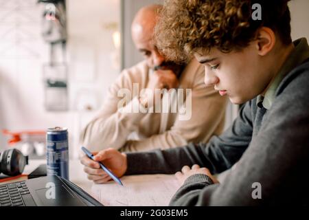 Boy doing homework while sitting by father at home Stock Photo