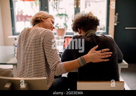 Mother sitting by teenage son studying at home Stock Photo