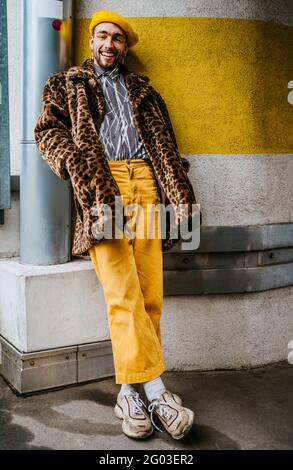 Full length of smiling young man with hands in pockets leaning on wall Stock Photo