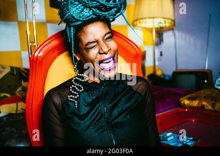 Portrait of cheerful woman winking while sitting on chair in living room Stock Photo
