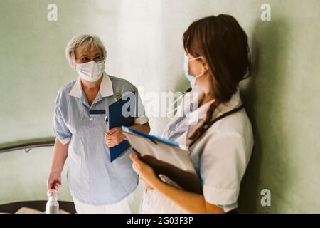 Female healthcare workers wearing face mask discussing at medical clinic during COVID-19 Stock Photo