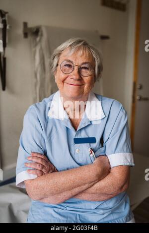 Portrait of smiling senior female doctor standing with arms crossed Stock Photo