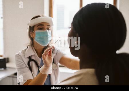 Female doctor wearing protective mask and face shield doing patient's medical test Stock Photo