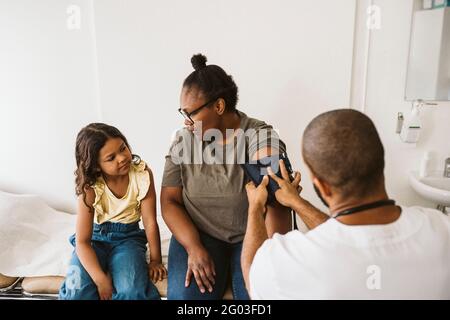 Mother talking with daughter while male doctor measuring blood pressure Stock Photo