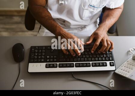 Male doctor typing on keyboard while sitting at desk Stock Photo