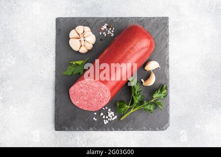 A loaf of salami Servelat sausage on a cutting Board with parsley and spices and garlic top view copy space Stock Photo