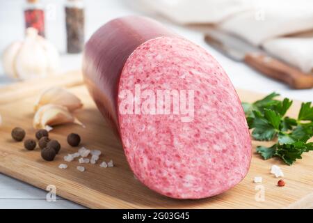 A loaf of salami Servelat sausage on a cutting Board with parsley and spices and garlic Stock Photo