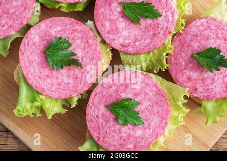 Sandwiches with lettuce leaves and sliced salami sausage on a wooden Board Stock Photo