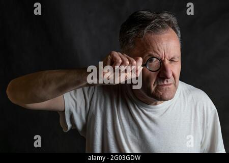 A man holds a magnifying glass in front of one eye looking through it with a very funny expression Stock Photo