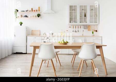 Dining room and stylish design. Wooden table and white chairs, kitchen utensils on furniture and small refrigerator Stock Photo