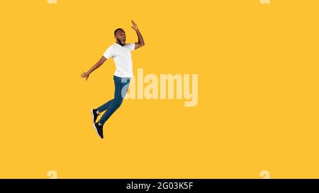 Black Guy Jumping Looking Aside In Shock On Yellow Background Stock Photo