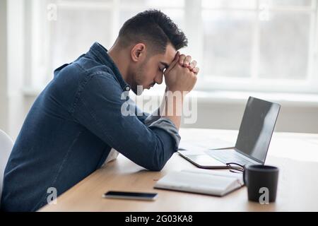 Depressed arab man sitting in front of laptop, office interior Stock Photo