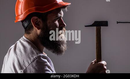 Hammer hammering a nail. Handyman services. Builders in hard hat, helmet. Bearded man worker with beard, building helmet, hard hat. Handyman, hammer Stock Photo