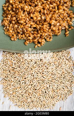 top view of raw whole rye grains and boiled porridge on green plate close up on wooden table Stock Photo