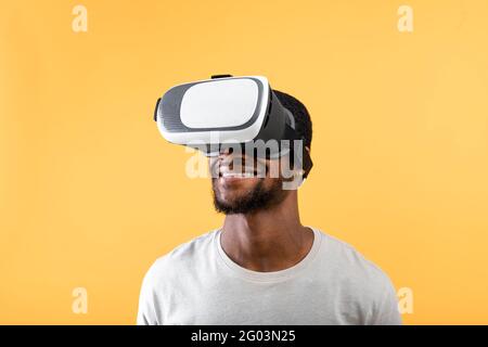 Modern technologies for entertainment. Happy african american man wearing vr glasses, standing on yellow background Stock Photo