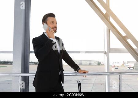 Cheerful businessman standing in airport, talking on phone Stock Photo
