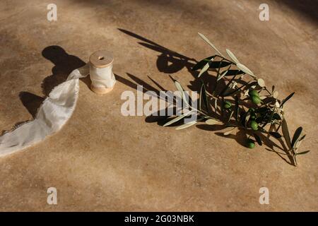 Summer wedding still life scene. Olive tree branch and silk ribbon on golden marble background in sunrise sunlight. Harsh long shadows. Moody Stock Photo