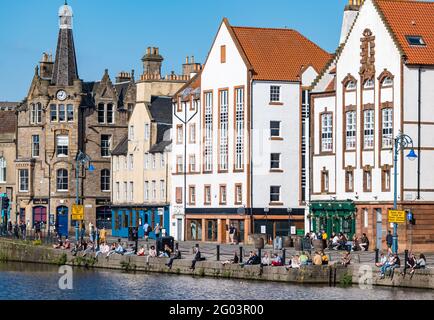 The Shore, Leith, Edinburgh, Scotland, United Kingdom, 31st May 2021. Leith bars busy: people enjoy drinks in the sunshine sitting on the riverbank on the Water of Leith on the last day of the bank holiday Stock Photo