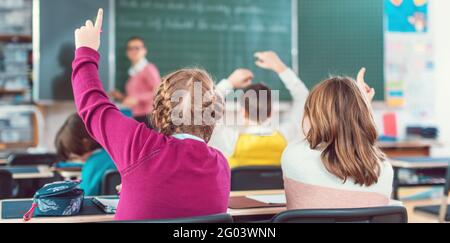 Two girl students raising hands to answer a question in school class Stock Photo