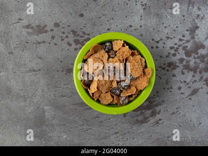 Top view of generic bran flakes with raisins in a green bowl isolated on a gray background. Stock Photo