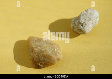 Beige and grey pebble stones at yellow sunny table. Stock Photo