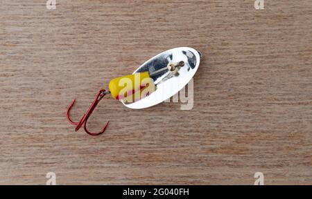 Generic yellow and red spots spinning fishing lure with a treble hook on a wood background. Stock Photo