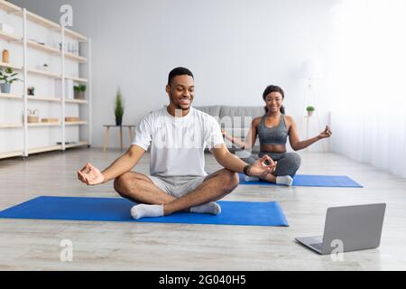 African Man Doing Yoga Online Meditating Sitting At Laptop Indoor