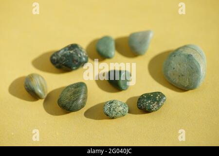 Set of green pebble stones at yellow sunny table. Stock Photo