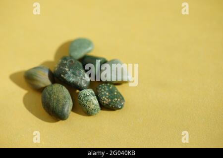 Heap of green pebble stones at yellow sunny table. Stock Photo