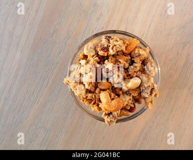 Top view of a small glass bowl filled with whole grains granola with fruit and nuts on a table. Stock Photo