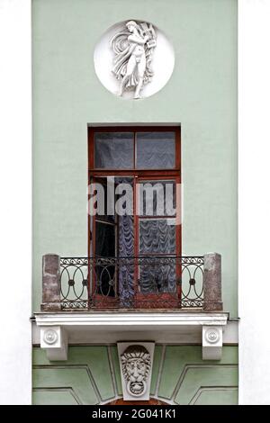 Balcony with a cast-iron fence and stucco molding, with an open balcony door against the background of a green wall with a bas-relief in a round niche Stock Photo