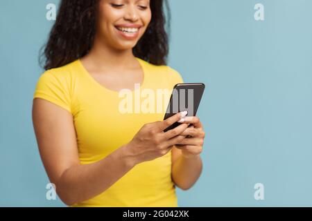 Chatting with friends. Happy black woman using smartphone texting sms message over blue background, selective focus Stock Photo
