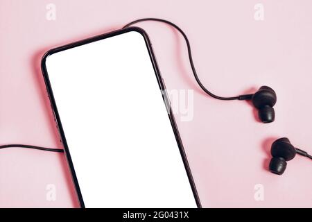 Smartphone mockup with blank white screen for trendy mobile application ad or demonstration. Headphones, pastel background. Social media application Stock Photo