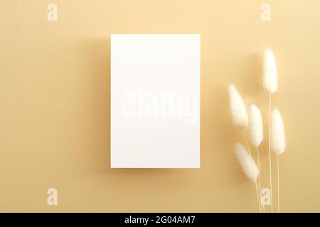 Vertical invitation card mockup with a lagurus on a beige table. Flat lay, top view. Stock Photo
