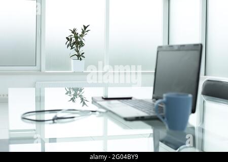 Laptop medical stethoscope coffee cup phone day planner on glass table in office space Stock Photo