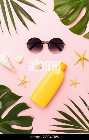 Sunglasses, sunscreen, seashells, chico leaves and monstera leaves on a pink background. Stock Photo
