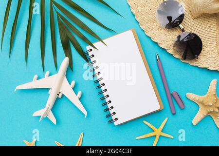 Blank notebook, pen, toy plane and sunglasses on blue background. Stock Photo
