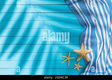 Towel and starfishes on blue wooden background with copy space and shadow from palm leaf. Stock Photo
