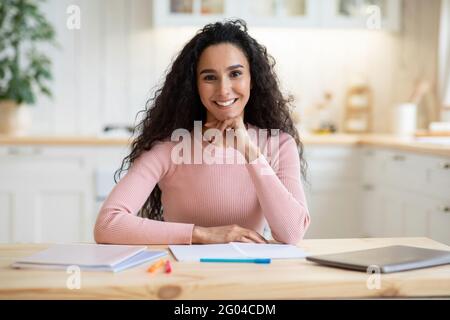 Work From Home. Smiling Beautiful Female Freelancer Sitting At Table In Kitchen Stock Photo