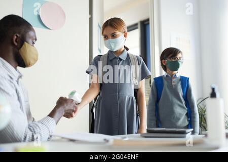 Portrait of male teacher checking temperature of children entering classroom in school, covid safety measures Stock Photo