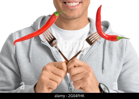 Young man holding forks with chili peppers on white background Stock Photo