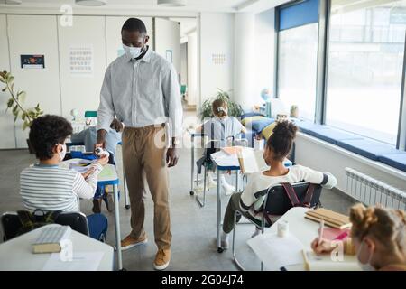 Full length portrait of African-American teacher sanitizing hands of children in school classroom, copy space Stock Photo