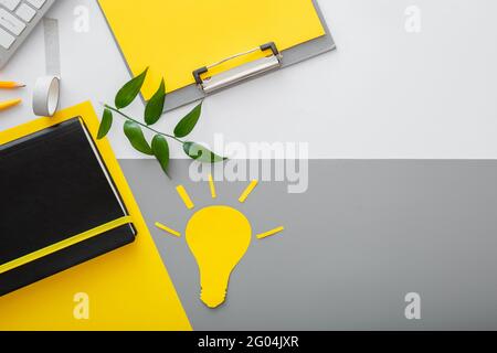 Yellow light bulb idea metaphor on desktop in workspace on gray table background with copy space. Stock Photo