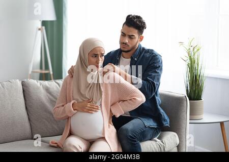 Caring arab husband making neck massage to pregnant muslim wife at home Stock Photo